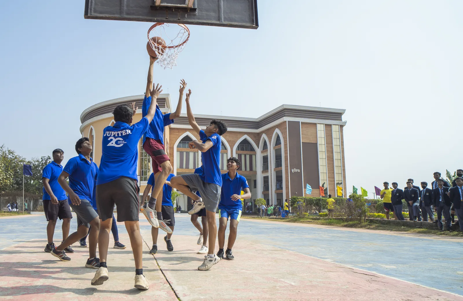 Students playing basketball on campus court with the main academic building facade behind.